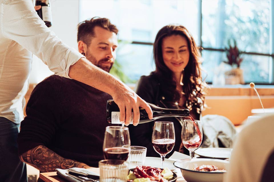 A picture of a man pouring wine for a couple who are on a date