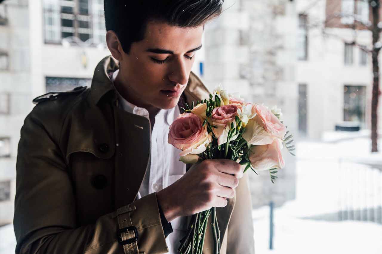  A man in a trench coat holding a bouquet of flowers.