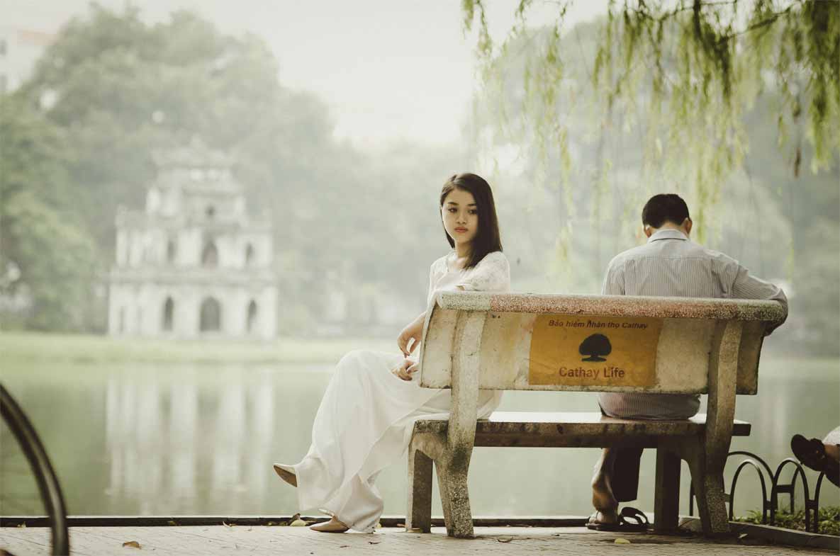 A photo of a couple sitting on a bench with the woman looking away from the man